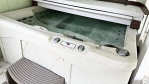 A hot tub with a control panel, a footrest, and a window in the background.