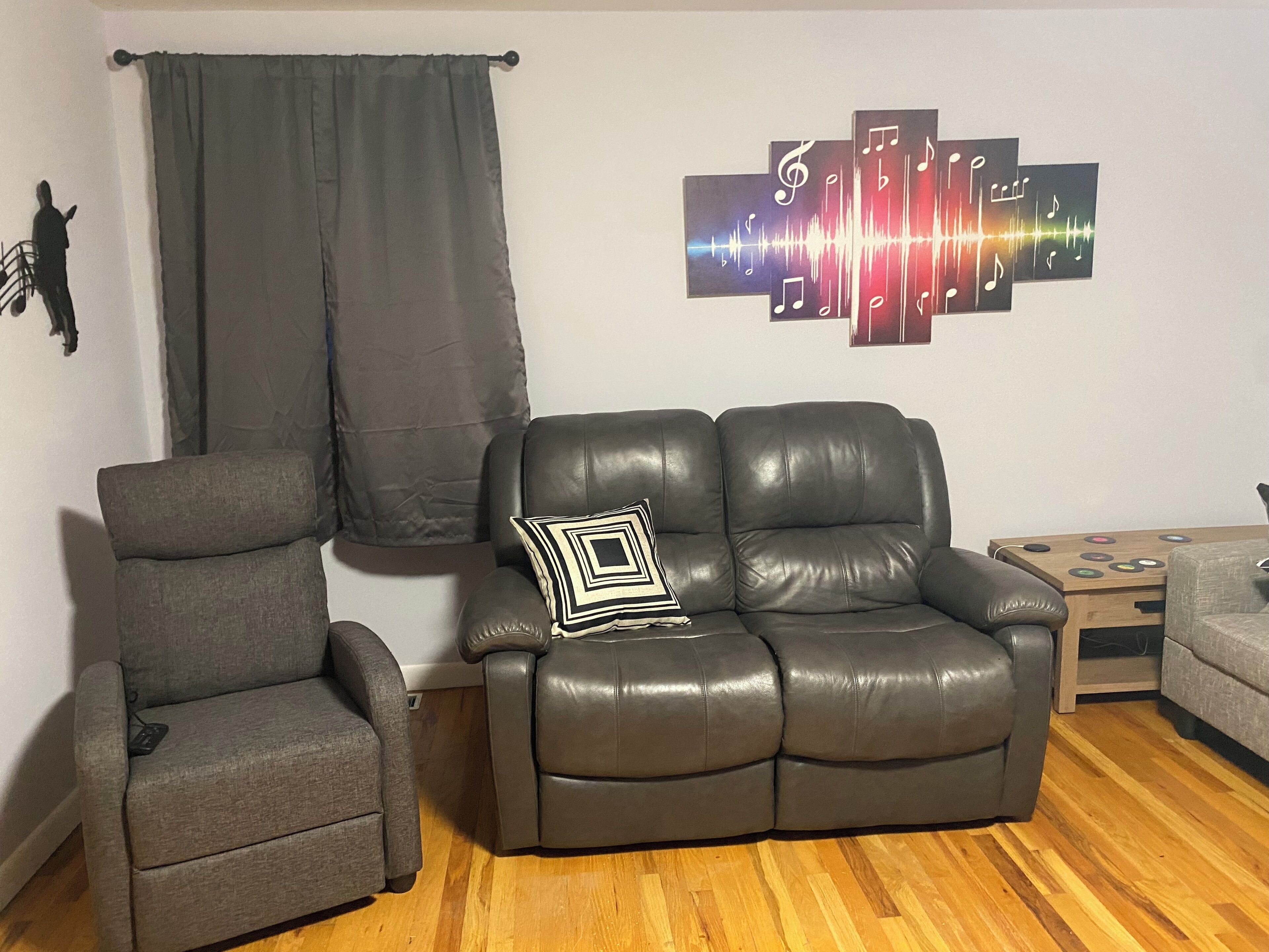 Ein Wohnzimmer mit grauem Sessel, einem Ledersofa mit geometrischem Kissen und einem Wandbild.