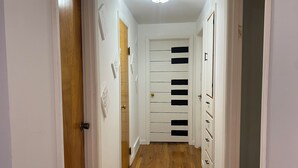 A narrow hallway with wooden flooring, white walls, and a door with black panels.