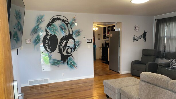 A living room with a grey sofa, wooden flooring, and a wall mural of headphones with music notes.