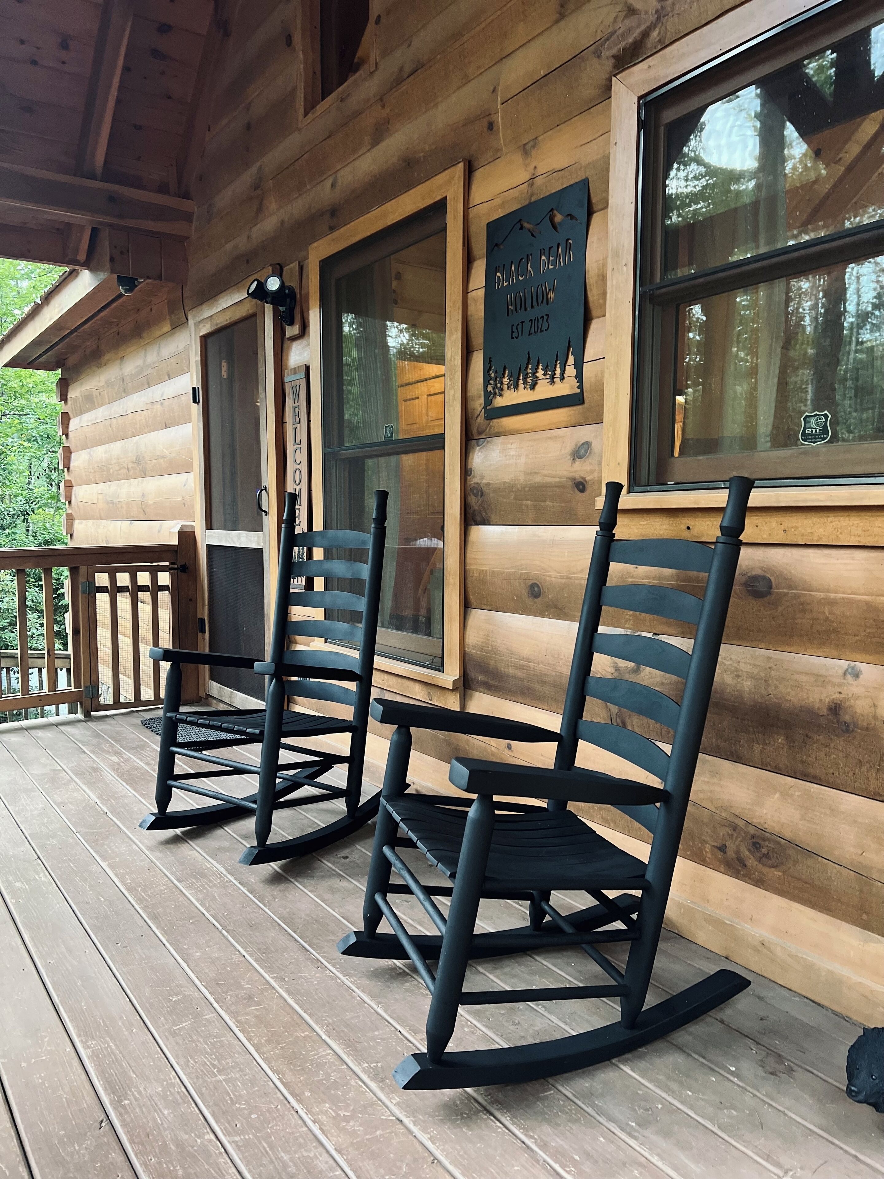 A wooden cabin with rocking chairs on the porch, a welcome sign, and a sign indicating the establishment year.