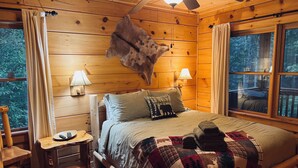 Camera accogliente con un letto di legno, due lampade sui comodini, un piccolo comodino, una finestra con tende e una ventola a soffitto.