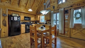 Interno di una baita in legno con cucina, tavolo da pranzo e sedie.