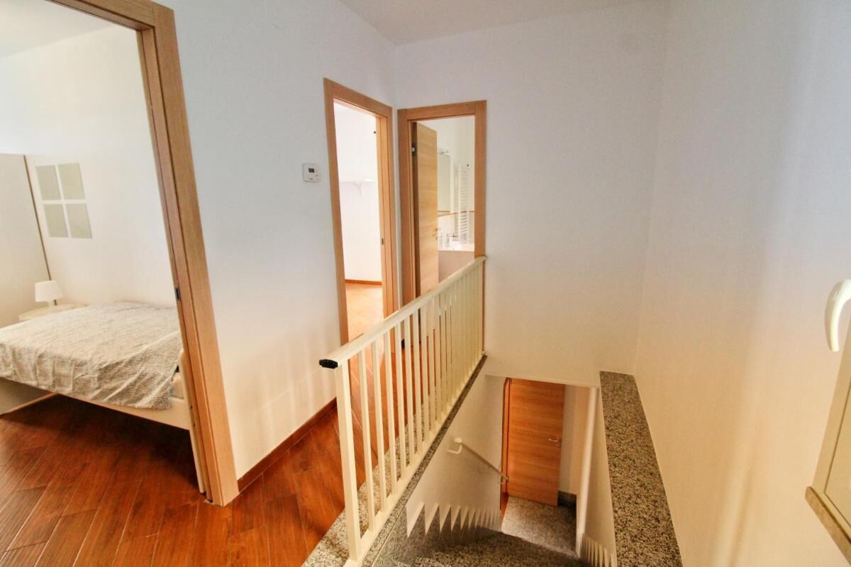 A room with a bed, wooden flooring, a white railing, and a view of a balcony.