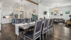 Une cuisine spacieuse équipée d’appareils électroménagers modernes, un coin repas avec une table et des chaises en bois, et un salon avec un canapé et un téléviseur.