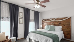 A bedroom with a wooden headboard, a bed with a white and green bedspread, a nightstand with a lamp, and a ceiling fan. - Century Cafe Flat (Kewaskum)