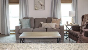 A living room with a sofa, a coffee table, and a chair. There is a lamp on a side table. - Century Cafe Flat (Kewaskum)
