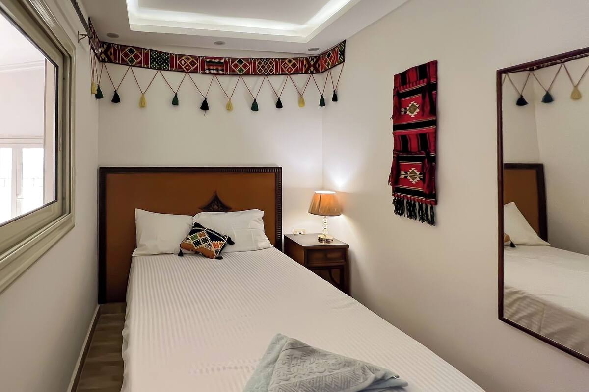 Ein Hotelzimmer mit einem großen Bett, einem Nachttisch mit Lampe, einem Fenster und einem Spiegel.