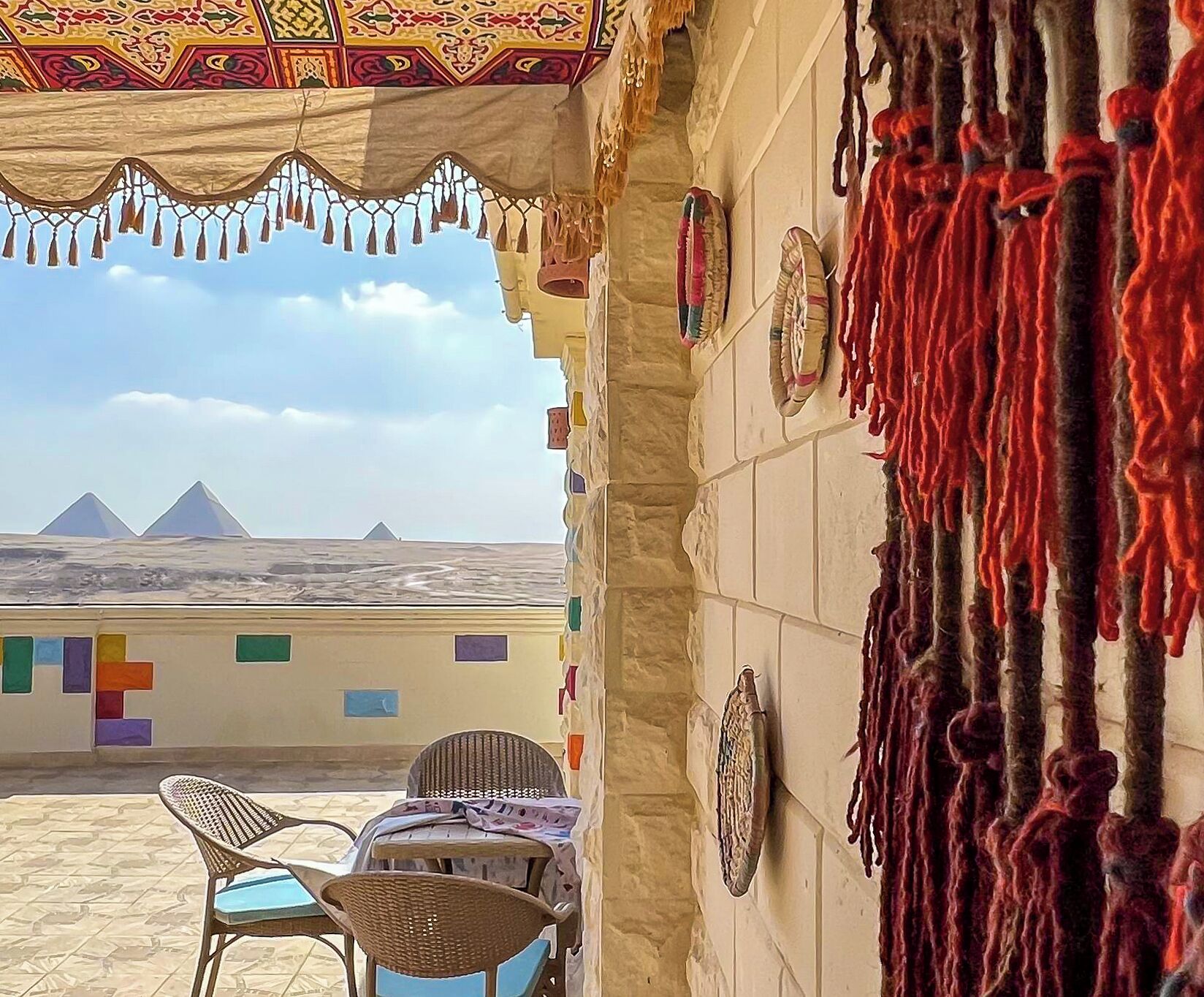 Una terraza con vistas a pirámides, techo con diseño y una pared decorada con objetos colgantes.