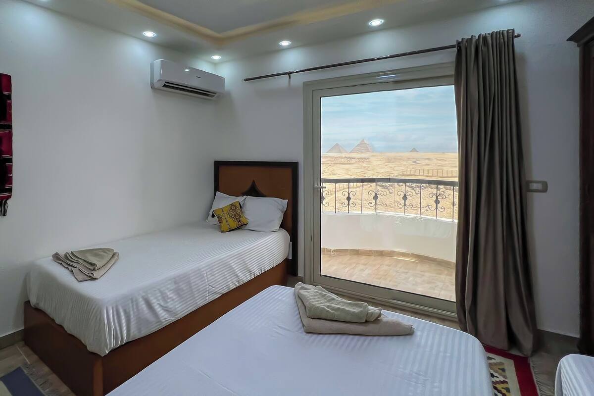 Ein Hotelzimmer mit Bett, einem Fenster mit Blick auf Pyramiden, einer Klimaanlage und einem Vorhang.