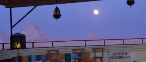 Vista del Atlantis Pyramids Inn con un letrero, área de asientos al aire libre y un cielo nocturno con la luna.