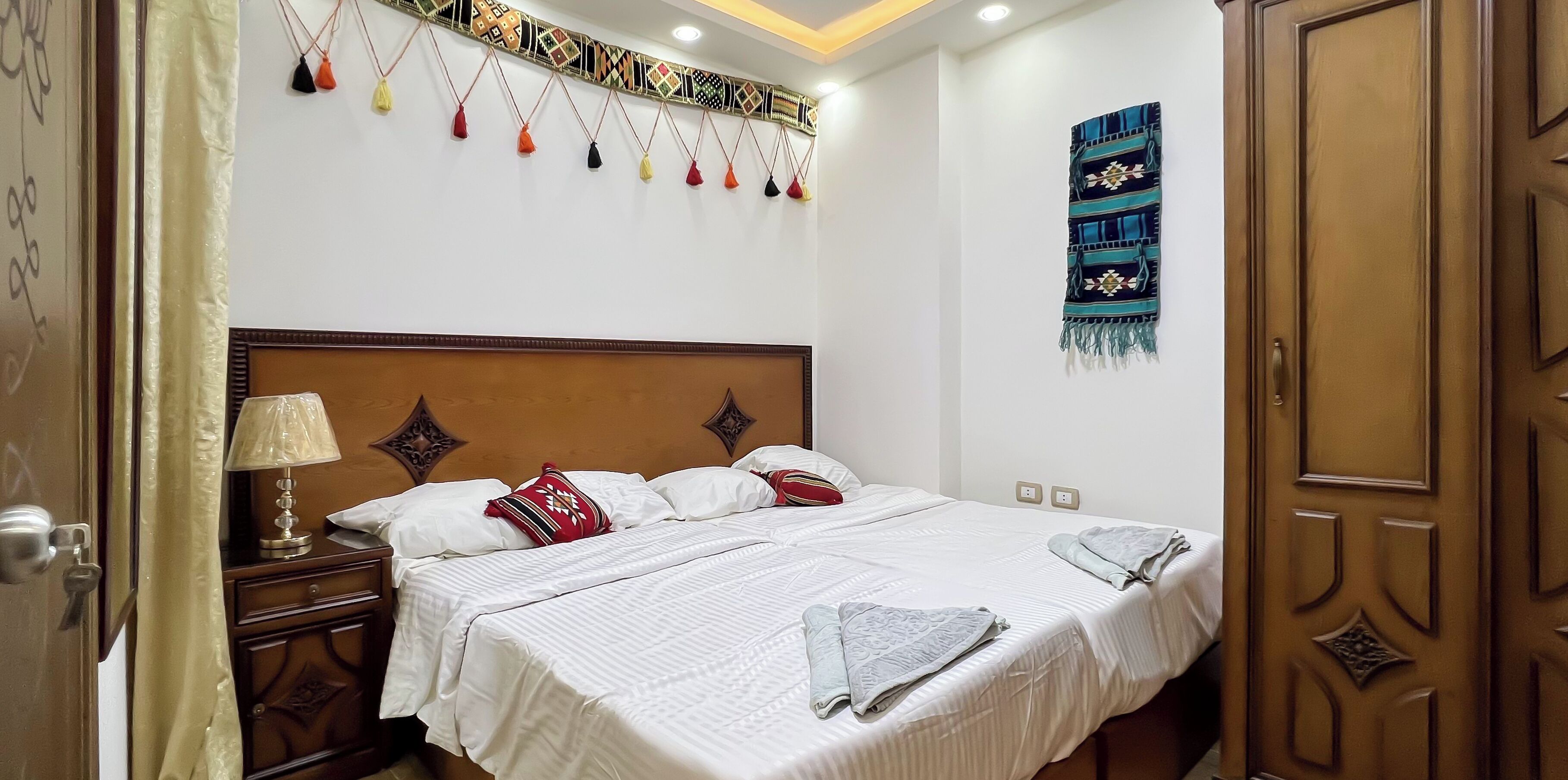 Une chambre d’hôtel avec un lit, une table de chevet, une lampe, un tableau ou une décoration murale, et une porte.