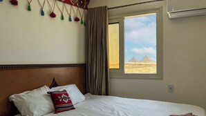 Una habitación de hotel con cama, una ventana que ofrece vistas a pirámides y una pared con borlas colgantes.