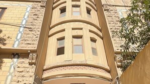 Un edificio con una escalera central que conduce a una entrada, rodeado de muros de piedra y varias ventanas.