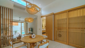 A modern dining area with a round wooden table, white wicker chairs, and woven pendant lights. - Villa Cocoon - Gaia (Canggu)
