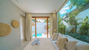 A bedroom with a large bed, a view of a swimming pool, and tropical plants. - Villa Cocoon - Gaia (Canggu)