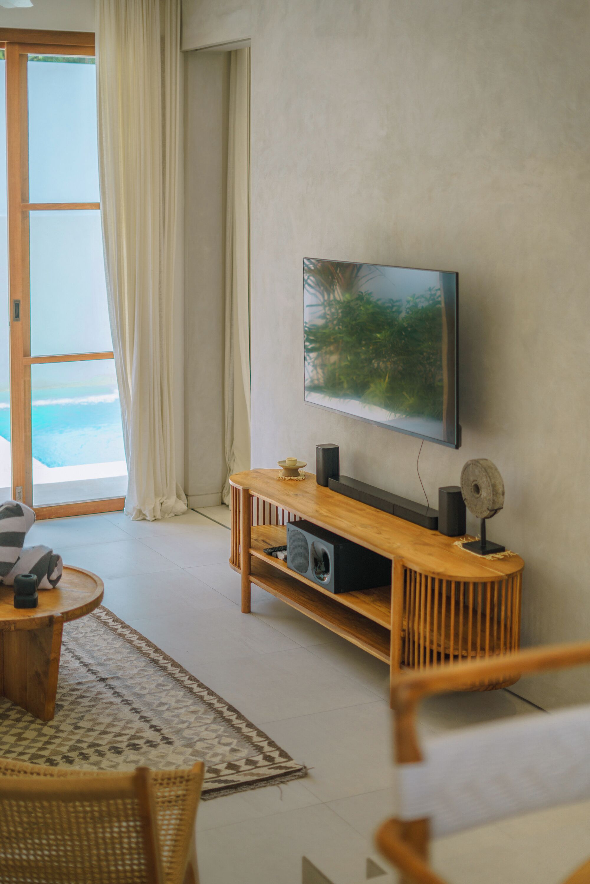 Un salon moderne avec un téléviseur à écran plat fixé au mur, un meuble de rangement en bois, une table basse ronde et un fauteuil en osier.