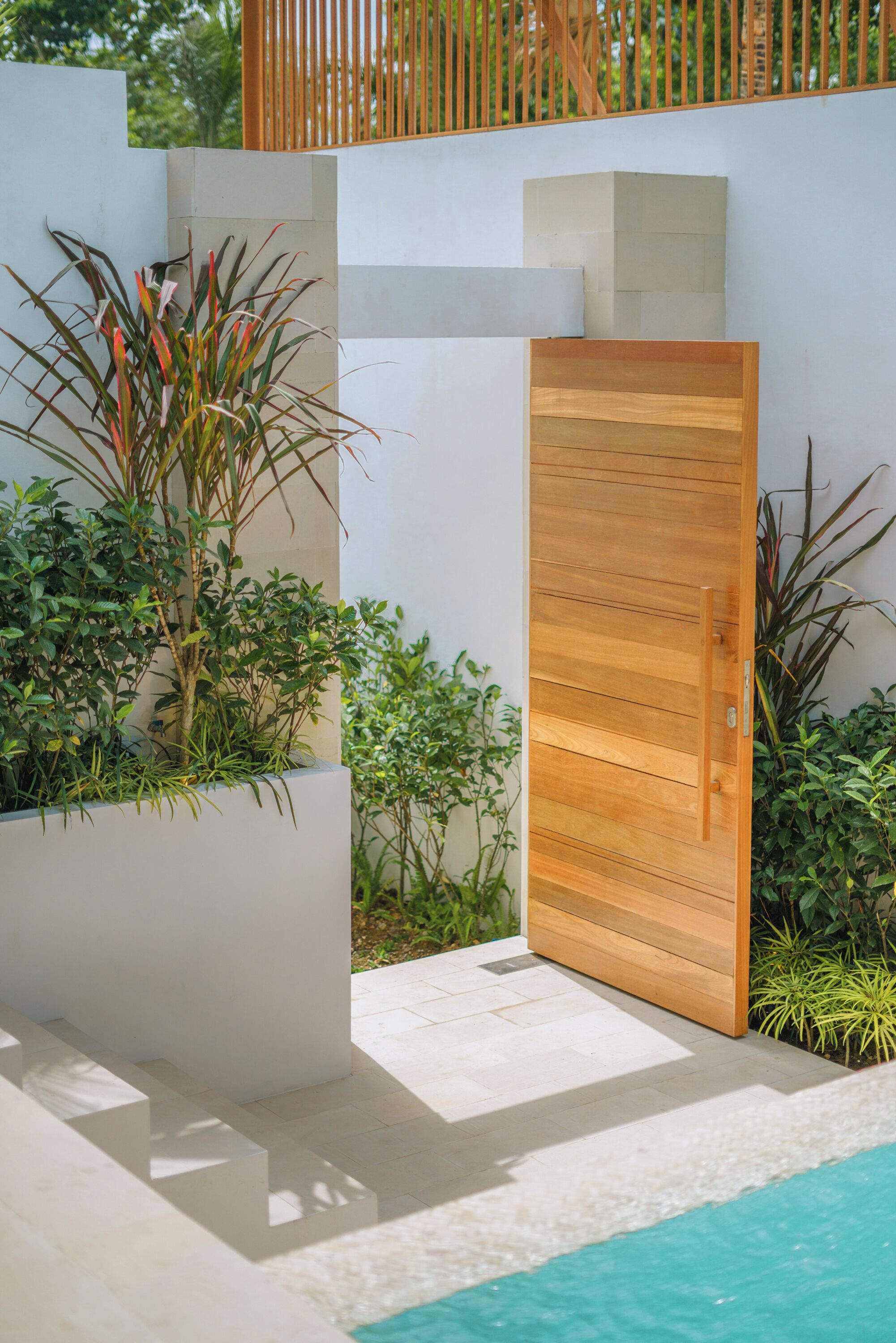 Un espace extérieur moderne avec une porte en bois, des murs blancs et une piscine.