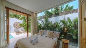 A spacious bedroom with a large bed, a view of lush greenery, and a pool area. - Villa Cocoon - Gaia (Canggu)