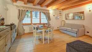 Een gezellige kamer met houten balken, een eettafel met stoelen, een bank en een radiator.