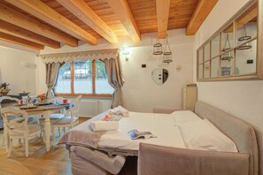 A room with a bed, a table with chairs, a window with curtains, and a mirror on the wall. - Cozy Nest in the old Town of Bardonecchia, Bardonecchia, Italy (Bardonecchia)