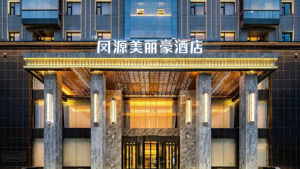 L’entrée d’un hôtel moderne, avec une façade imposante, de grandes colonnes et un hall d’entrée bien éclairé.