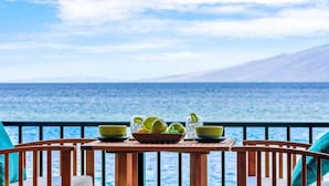 Una mesa de madera con cuencos y vasos en un balcón con vista al mar.