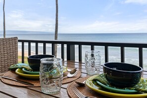 Une table dressée avec des assiettes, des bols et des verres, placée sur une terrasse en bois donnant sur l’océan.