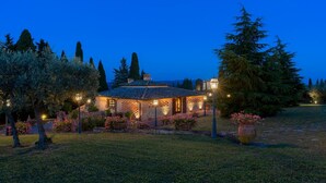 A villa with a tiled roof, surrounded by a garden with flowering plants and trees.