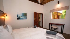 A bedroom with a bed, a desk, a chair, a painting, and a window with a view of greenery. - 2 bed Apartment With Pool - 2126 (Victoria Falls)