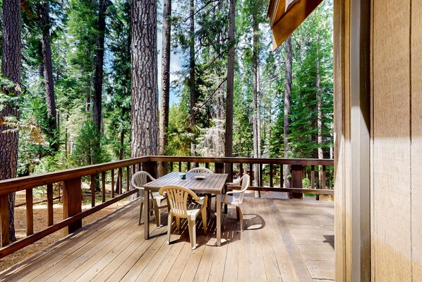 Una terraza de madera con una mesa y sillas, rodeada de árboles altos.
