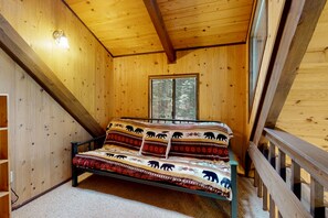 Una habitación de cabaña de madera con una cama, una ventana y una escalera de madera.