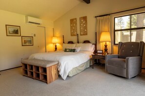 A bedroom with a bed, bedside lamps, a chair, a wooden bench, and artwork on the walls.