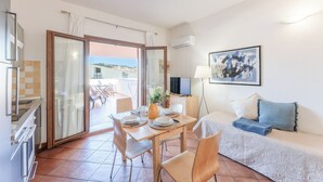 A dining area with a table set for four, a sofa, a TV, and a painting on the wall. - Relaxing Cristal Bedroom Apartment Sleeps Num1502 (Santa Teresa di Gallura)