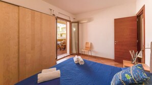 A bedroom with a bed, a chair, a wooden wardrobe, and a door. - Relaxing Cristal Bedroom Apartment Sleeps Num1502 (Santa Teresa di Gallura)