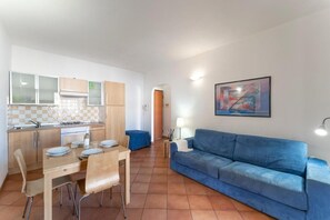 Un espace de vie compact comprenant une kitchenette, un coin repas et un canapé bleu.