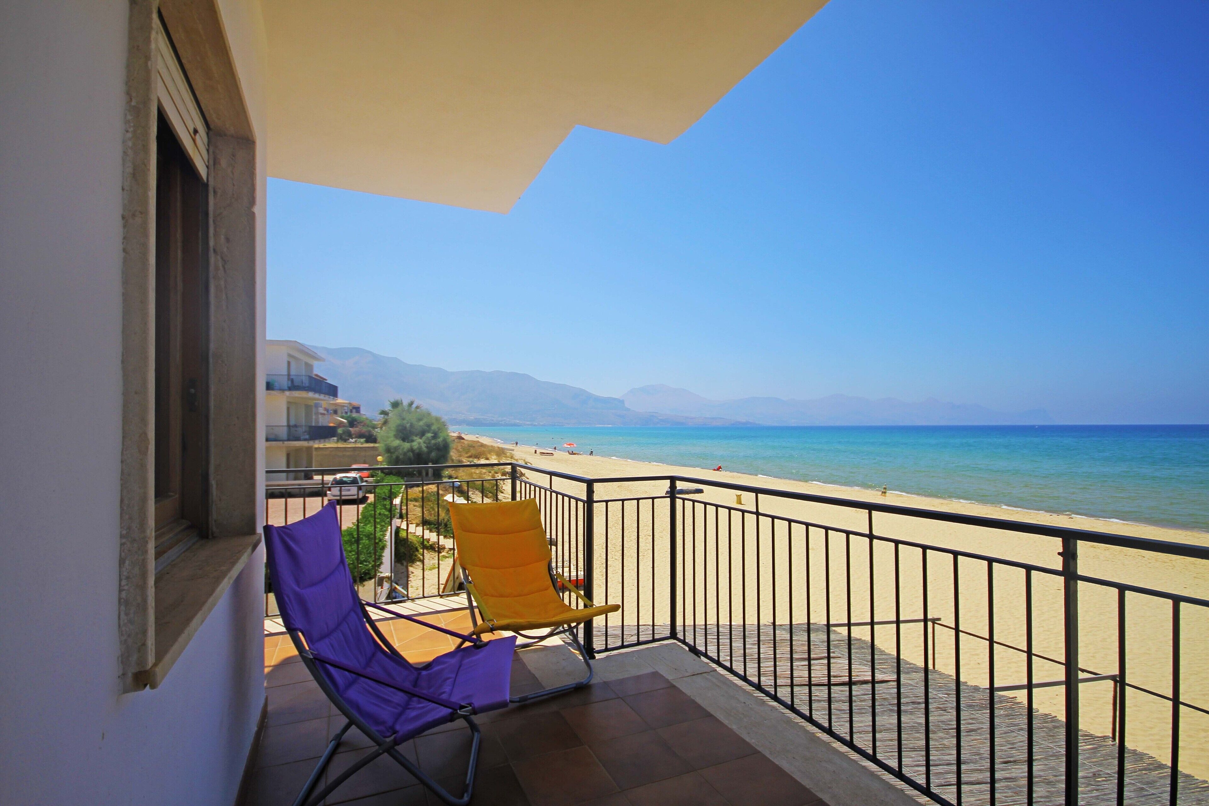 A balcony with two chairs and a view of the beach and mountains.