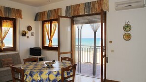 A dining area with a table set for four, a ceiling fan, and a view of the sea through a sliding glass door. - Gorgeous Beach House (Alcamo)