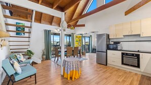 Una cocina amplia con vigas de madera, un comedor con mesa y sillas, y vistas a través de puertas de cristal.