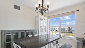 Une cuisine avec une grande table en bois, des placards blancs et une fenêtre donnant sur des maisons.