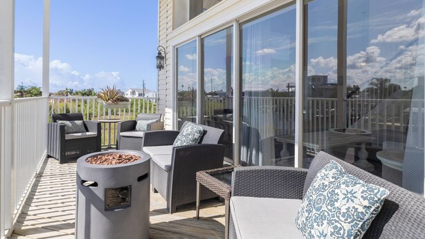 Une terrasse extérieure avec des meubles en osier, un foyer et une structure en verre.