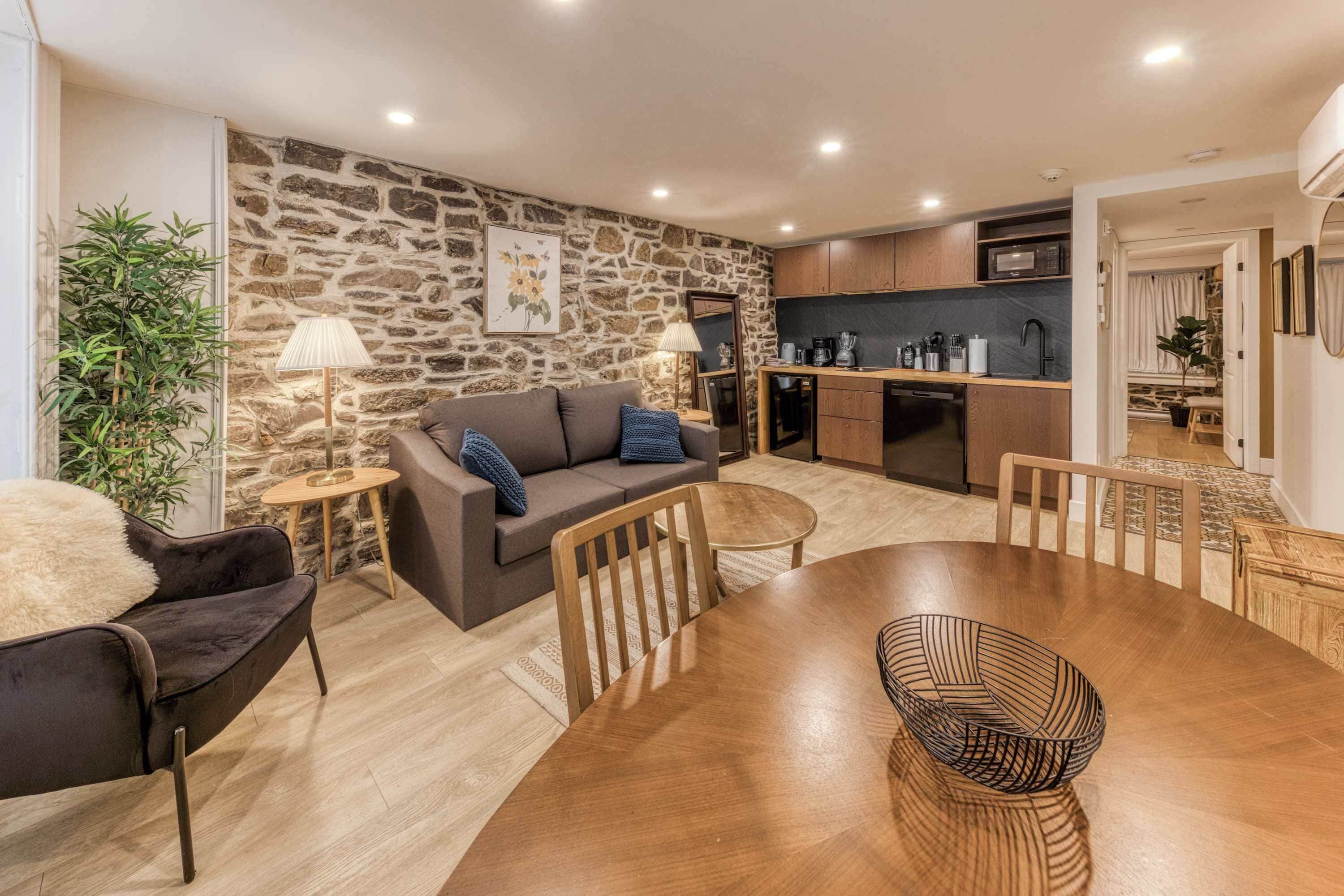 A cozy living area with a stone wall, a sofa, a dining table, and a kitchen in the background.