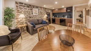 Un área de estar acogedora con una pared de piedra, un sofá, una mesa de comedor y una cocina al fondo.