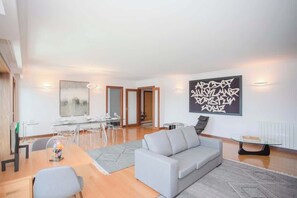 A modern living room with a grey sofa, a glass coffee table, and a dining area with a glass table and chairs.