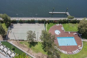 Vista aérea de uma propriedade com quadra de basquete, piscina e um cais que se estende sobre a água.