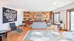 Ein modernes Wohnzimmer mit einer Couch, einem Esstisch für vier Personen und einer an der Wand befestigten Holzregal mit verschiedenen Gegenständen.