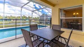 Un espace extérieur abrité comprenant une piscine, une table avec des chaises et une vue sur un lac et des bâtiments en arrière-plan.
