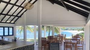Un restaurante con barra de piedra, mesas y sillas de madera, con vistas a una playa y al océano.