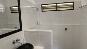 Un baño moderno con un espejo grande, un lavabo de piedra, una bañera y una zona de ducha.