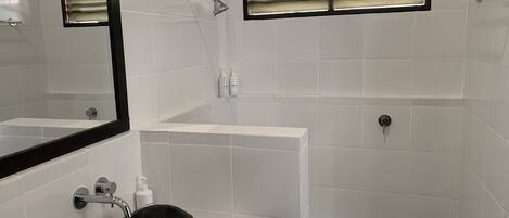 Une salle de bain moderne avec un grand miroir, un lavabo en pierre, une baignoire et un espace douche.